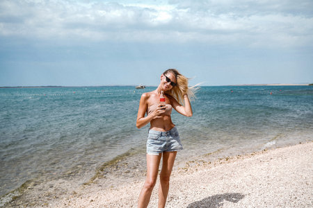 Summer photo of blonde happy woman relaxing on the beach, smiling. Girl with fit tan body wearing short jeans. Tourism. Travel.の写真素材