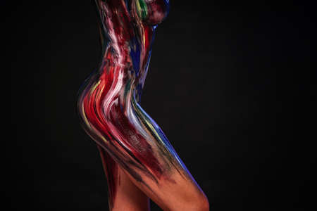 Body part art. Photo of female sensual creative body in colorful paints on a black studio background. A lot of copy space.の写真素材