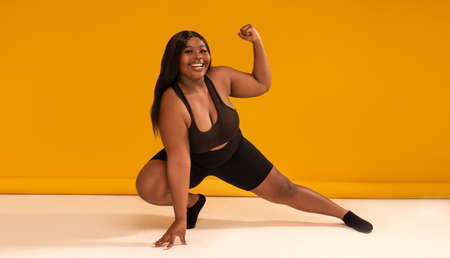 Happy plus size woman posing in sporty black fashionable clothes, smiling to the camera. Copy space. Sports and weight loss concept. Studio shot. Full length photo.の写真素材