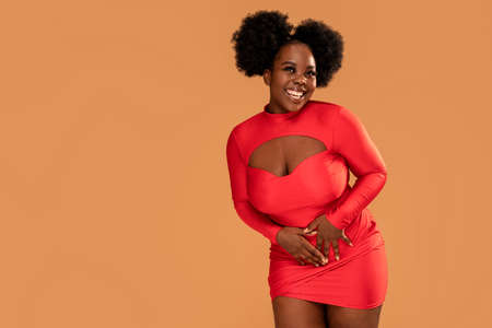 Happy afro Woman posing in fashionable red mini dress, looking at the camera and smiling. Glamor makeup. Date time. Studio Background. A lot of copy space.の写真素材