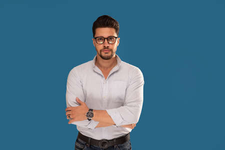 Fashionable young businessman posing on the blue studio background. Copy space. Bearded man wearing eyeglasses looking at the camera.の写真素材