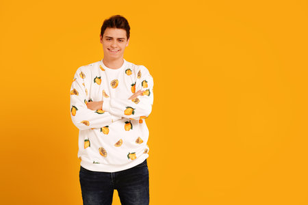 Young smiling handsome man in fashionable clothes posing isolated on yellow studio background, looking at the camera. Real people emotions and lifestyle concept. Copy space.の写真素材