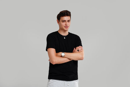 Handsome young man posing in black fashionable shirt, hand watch and jewelry, looking at the camera. Student. Studio shot. Gray background. Copy space.の写真素材