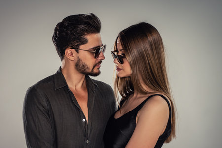 Portrait of young handsome couple wearing fashionable sunglasses, looking at eachother. Studio background. Bearded man posing with beautiful woman.の写真素材