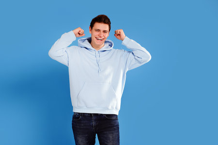 Caucasian young male student posing with big smile on blue studio background. Victory, success. Real human emotions concept.の写真素材