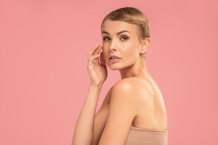 Delicate caucasian woman with blonde short hair and natural makeup looking at the camera. Fashionable haircut. Beauty portrait. Studio pink pastel background.の写真素材