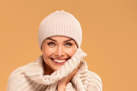 Portrait of beautiful happy woman with delicate makeup and big amazing smile, wearing beige cap and warm scarf, looking at camera. Studio background. Autumn, winter style. Real people emotions concept.の写真素材