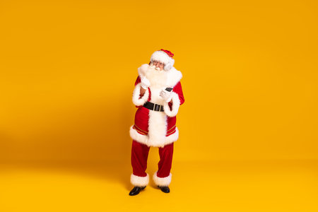Happy bearded real Santa Claus with headphones dancing and listening music from mobile phone. Yellow studio background. Christmas time. Copy space. Xmas vibes.の写真素材
