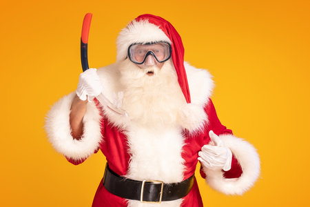 Funny photo of real Santa Claus wearing diving mask, posing over yellow studio background. Xmas vibes. Christmas happy time.の写真素材