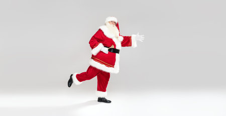 Christmas are coming! Real Santa Claus ringing the bell and running over light gray studio background, looking at the camera. Xmas sale, discount concept. A lot of copy space.の写真素材