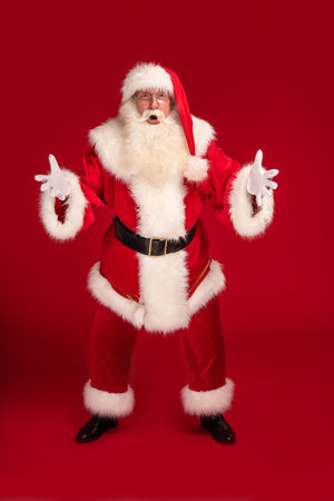 Full length photo of real, happy Santa Claus annoucing big xmas sale on a red studio background. Merry Christmas and Happy New Year!の写真素材