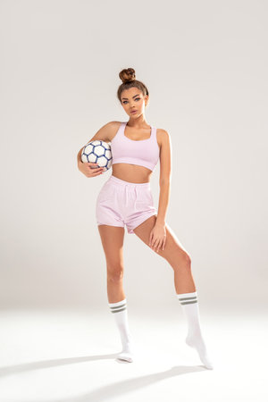 Beautiful brunette girl in fashionable sportswear holding football ball, looking at camera, waiting for the soccer competition, championship. Copy space. Hobby. Sport.の写真素材