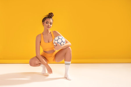 Attractive female brunette girl in fashionable sportswear and stockings posing with football ball, looking at camera, waiting for the soccer competition, championship. Copy space. Hobby. Sport.の写真素材