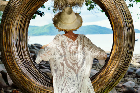 Summer beach vacation concept. Back view of happy woman with hat relaxing on the swing. Island vibes. Tropical destination. Paradise. Thailand, Asia.の写真素材