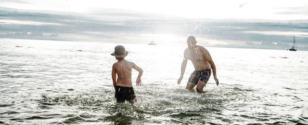 Happy father playing with little son in the water, splashing, having fun together. Daddy with kid on the beach. Family vacation. Summer vibes.の写真素材