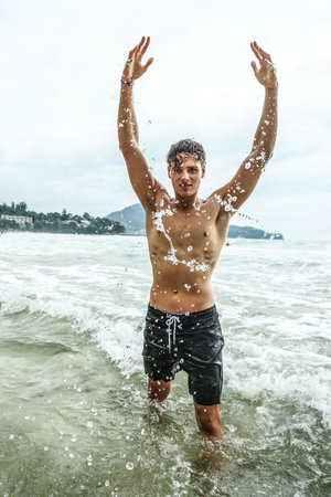 Young fit man having fun in the water, sunny summer day outdoor at the beach. Boy with fit body.の写真素材