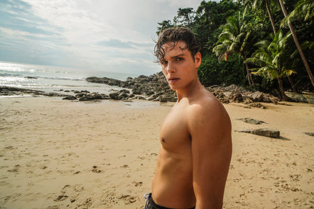 Handsome young fit man posing on the tropical beach, looking at the camera. Summer vibes. Wanderlust.の写真素材