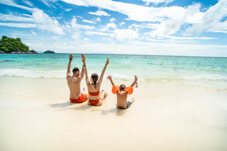 Photo of a happy family on tropical vacation, having fun on the tropical beach, playing with sea water. Little boy with parents. tourists.の写真素材