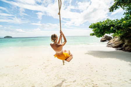 Happy woman on the tropical beach having fun on swing, sea shore during summer vacations. copy space. Traveler. tourists. Wanderlust. Real people lifestyle.の写真素材