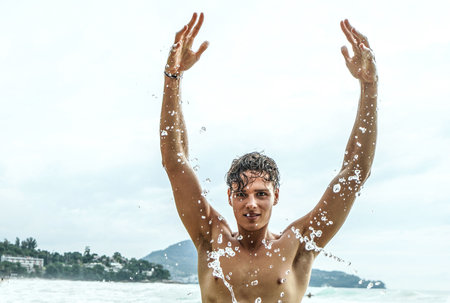 Happy young man having fun in the sea, splashing water with his hands. Summer. Travel. Tourism. Freedom.の写真素材