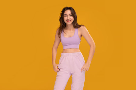 Studio photo of a happy, relaxed, young brunette woman in sporty clothes posing over yellow background with big smile, looking at the camera. female student. A lot of copy space.の写真素材