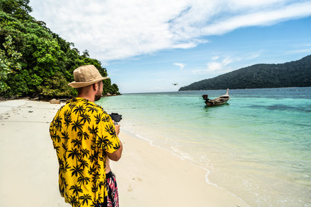 Drone flying at sunny day over the sea, at the tropical little beach. Man landing the drone. Summer vibes. Hobbies concept.の写真素材