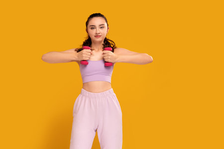 Young fitness woman in fashionable sporty clothes posing on the yellow studio background. A lo of copy space. Healthy lifestyle concept. Beautiful active student girl.の写真素材