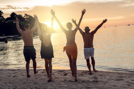 Group of happy friends enjoying beautiful sunset at the tropical beach, jumping and having fun together. Travelers. tourism. back view. Thailand, Asia.の写真素材