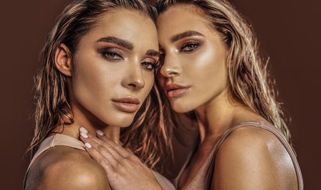 Beauty photo of two sexy twins sisters looking at the camera. Perfect face makeup. golden colors. studio shot.の写真素材