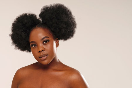 Beauty portrait of attractive woman with afro hair looking at the camera, posing over studio background. Girl with long lashes and delicate makeup. A lot of copy space.の写真素材