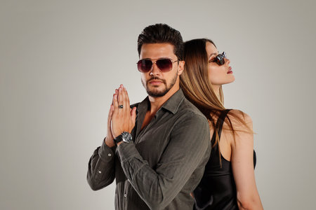 Fashion photo of handsome young couple posing together in studio, wearing summer sunglasses. Elegant man with beard and attractive woman with long hair. personal accessories. copy space. Gray background.の写真素材