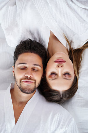 Top view portrait of cheerful, romantic couple in love, lying on bed with smile. Beautiful wife with handsome man. date.の写真素材