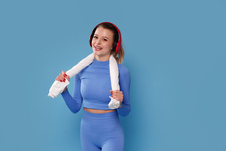 Sports Happy Model. Young Fit Woman Wearing Wireless Headphones Posing Over blue studio pastel Background. A lot of copy space.の写真素材