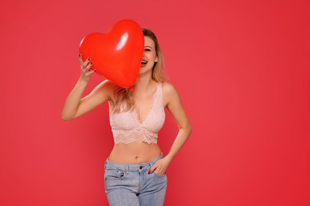 Happy woman with heart red balloon laughing and having fun, standing on the red studio background. Self love, skin care concept. copy space.の写真素材