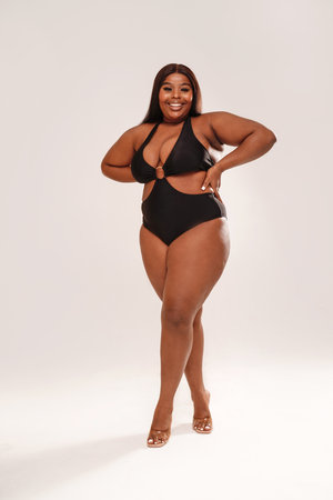 Full length photo Of Curvy Smiling African American Woman posing in black swimsuit. studio shot. body positive.の写真素材