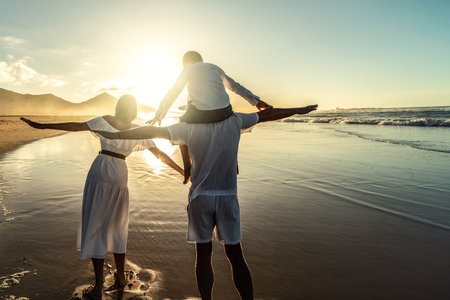happy family. Mom, dad and son walking together on the tropical beach, having fun. back view. sunset light. summer holiday. Travelers. tourists.の写真素材