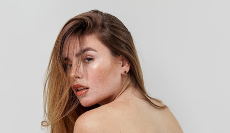 Beauty portrait of charming caucasian young woman with natural freckles on her face and shoulders. Girl looking at the camera. Delicate elegant small earrings in ear. A lot of copy space.の写真素材