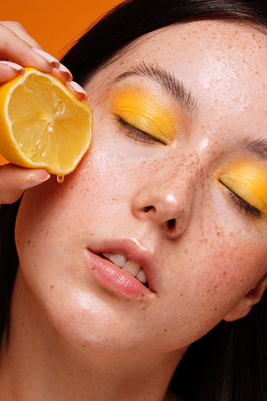 Beauty woman squeezing juicy lemon fruit on her healthy skin with natural freckles . Concept of a clean skin care, cosmetology.の写真素材
