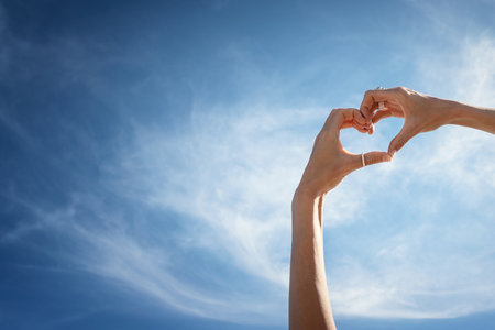 Conceptual photo of female's hands making heart against blue sky. A lot of copy space.の写真素材