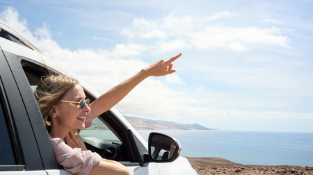 Smiling, excited woman in sunglasses sitting in car and pointing the sky during trip on the island. Real people lifestyle. Traveler. Wanderlust. tourism concept.の写真素材
