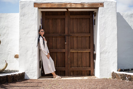 Relaxed woman standing near big wooden door, enjoying summer vacation day at the spanish island. tourism. Traveler.の写真素材