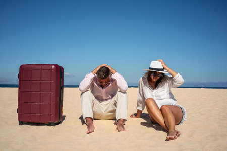 Lost couple of travelers sitting sad on the sandy beach with a big suitcase. concept photo. copy space. tourism.の写真素材
