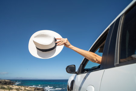 Women hand holding white hat outside open car window. travel concept. dream. Wanderlust. tourism. copy space.の写真素材