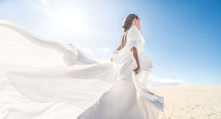 Photo of a woman in amazing white wedding dress posing on the desert, sunny light, blue sky, beautiful pastel tone, copy space.の写真素材