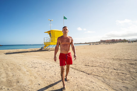 Handsome man walking relaxed on the sandy beach after swimming in the ocean. lifeguard. Summer vibes. tourists.の写真素材