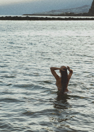 Freedom. Vintage style photo of a girl relaxing and swimming in the ocean water after the sunset. Wanderlust. hippie life. back view.の写真素材