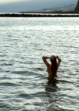 Freedom. Photo of a girl relaxing and swimming in the ocean water after the sunset. Wanderlust. hippie life. back view.の写真素材
