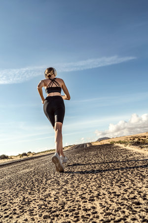 Back view of young fit female running at sunny day, morning light. Motivation, fitness and healthy lifestyle concept.の写真素材