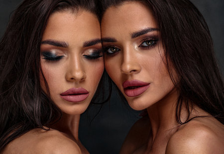 Beauty photo of two sexy women with glamor makeup. One girl is looking at the camera, the second one has closed eyes. Closeup portrait.の写真素材