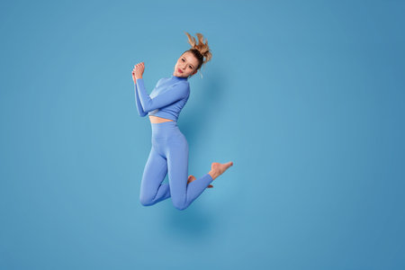 Happy, sporty woman in fashionable sportswear jumping on blue studio background. Sport and healthy lifestyle. A lot of copy space.の写真素材